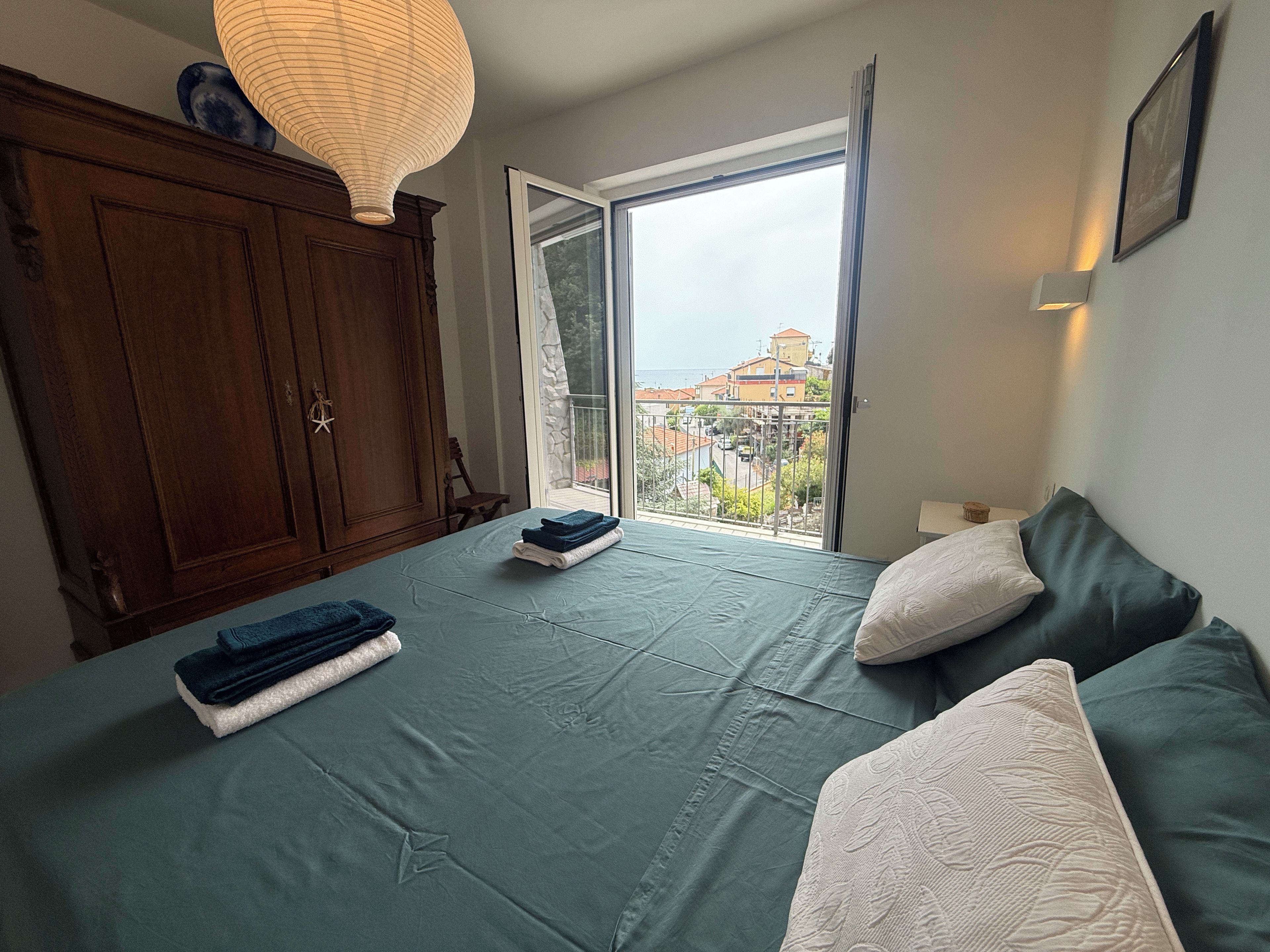 Quarto com cama, guarda-roupa de madeira, janela com vista para edifícios e luminária no teto.