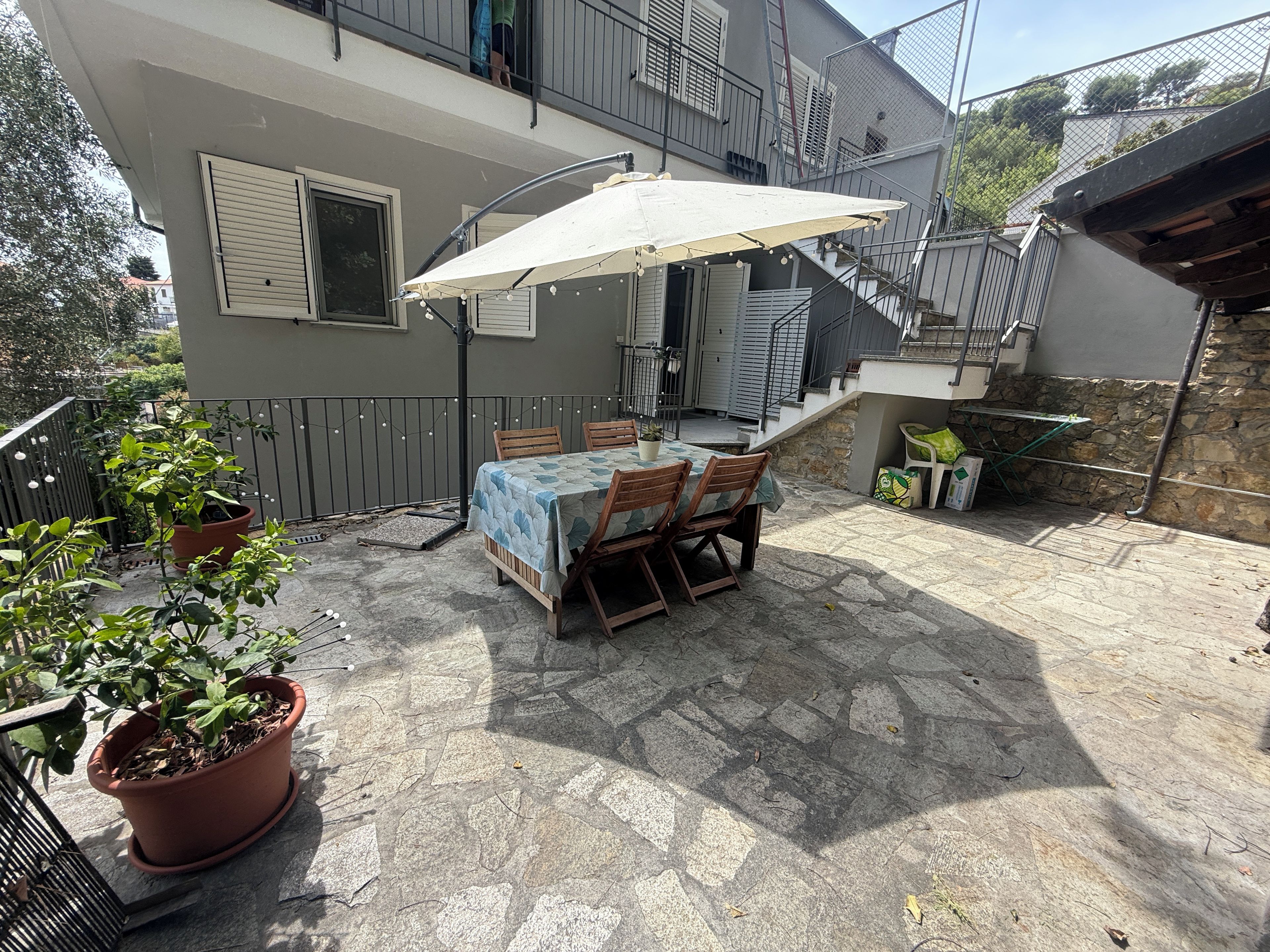 Een terras buiten met een tafel en stoelen, omgeven door potplanten.