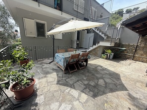 Een terras buiten met een tafel en stoelen, omgeven door potplanten.