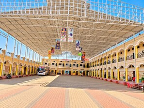 A covered outdoor area with a bus, potted plants, and a tiled floor. - Athithi Bhawan (Khandwa)