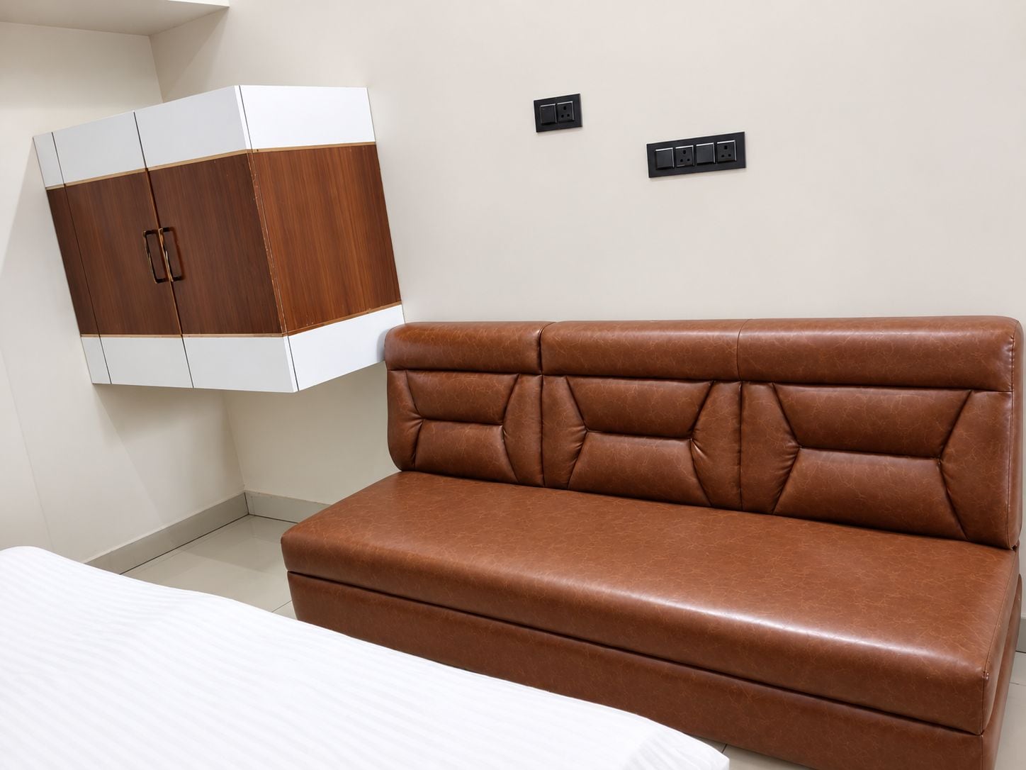 Een kamer met een bruine leren bank, een wit bed en een houten garderobe.