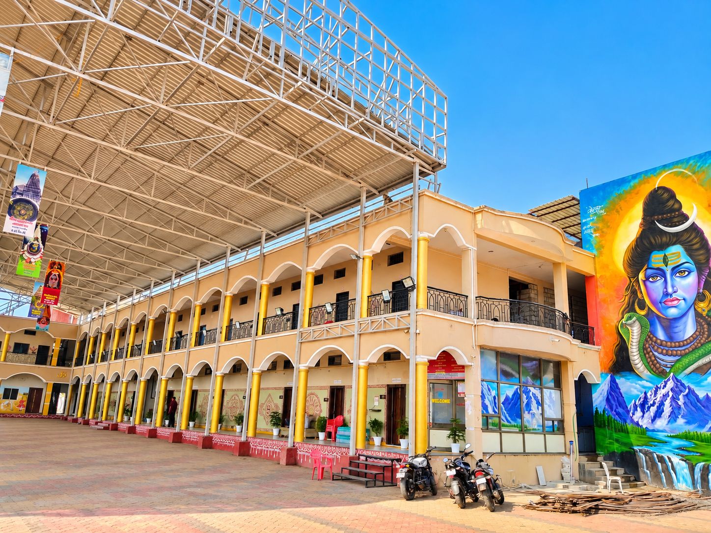 Un edificio de varios pisos con un patio central cubierto, un mural a la derecha y una fila de motocicletas estacionadas.