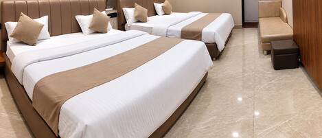 A hotel room with three beds, a wooden wardrobe, and a small seating area.