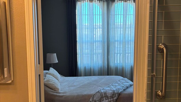 Hotellihuone, jossa on sänky, yöpöytälamppu ja ikkunasta avautuva näkymä, jonka edessä on verhot.