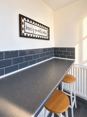 A kitchen with a black and white backsplash, a grey countertop, and two wooden stools. - Stylish 4BR Sunderland | Contractor Friendly (Sunderland)