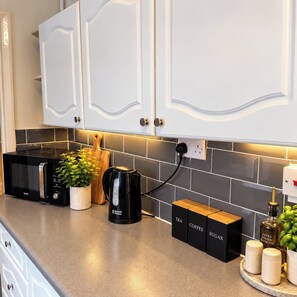 A kitchen with white cabinets, a black coffee maker, a kettle, and labeled containers for tea, coffee, and sugar. - Stylish 4BR Sunderland | Contractor Friendly (Sunderland)