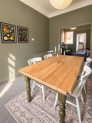 A dining room with a wooden table and white chairs, framed botanical prints on the wall, and a patterned rug. - Stylish 4BR Sunderland | Contractor Friendly (Sunderland)