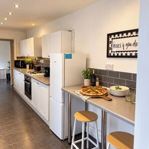 A modern kitchen with white cabinets, a stainless steel refrigerator, a pizza on the counter, and a bar stool. - Stylish 4BR Sunderland | Contractor Friendly (Sunderland)
