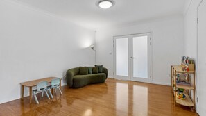 A spacious room with a wooden floor, a green sofa, a small table with chairs, and a bookshelf with children's books. - Pottsville Paddock - Private pool, sauna, home gym, close to the beach & creek and bring the pets (Pottsville)