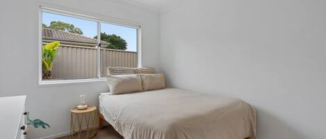 A bedroom with a bed, a bedside table, a lamp, and a window.