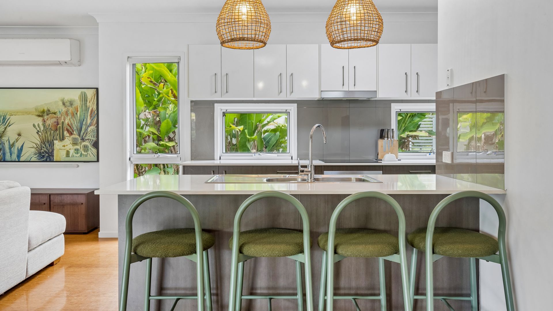 Une cuisine moderne avec des meubles blancs, un îlot central doté de tabourets et des luminaires suspendus.