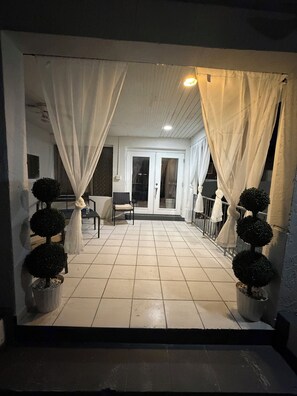 A covered outdoor area with a tiled floor, white curtains, and potted topiary plants. - House with a pool, 5 minutes from Miami Airport (Hialeah)