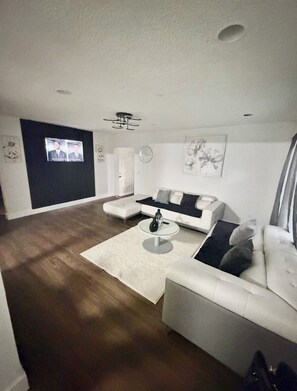 A modern living room with a sectional sofa, a coffee table, and a flat-screen TV mounted on the wall. - House with a pool, 5 minutes from Miami Airport (Hialeah)
