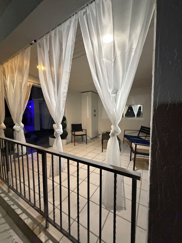 Un balcon avec des rideaux blancs, un sol carrelé et une balustrade.