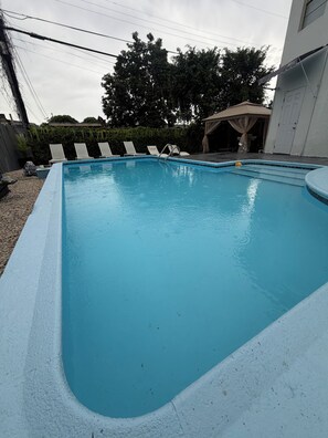 A rectangular swimming pool with a blue interior, surrounded by a white deck. There are lounge chairs aligned along the pool's edge. - House with a pool, 5 minutes from Miami Airport (Hialeah)