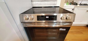 A stainless steel range with a digital display and four knobs, located in a kitchen with white cabinetry and a wooden floor.