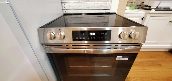 A stainless steel range with a digital display and four knobs, located in a kitchen with white cabinetry and a wooden floor.