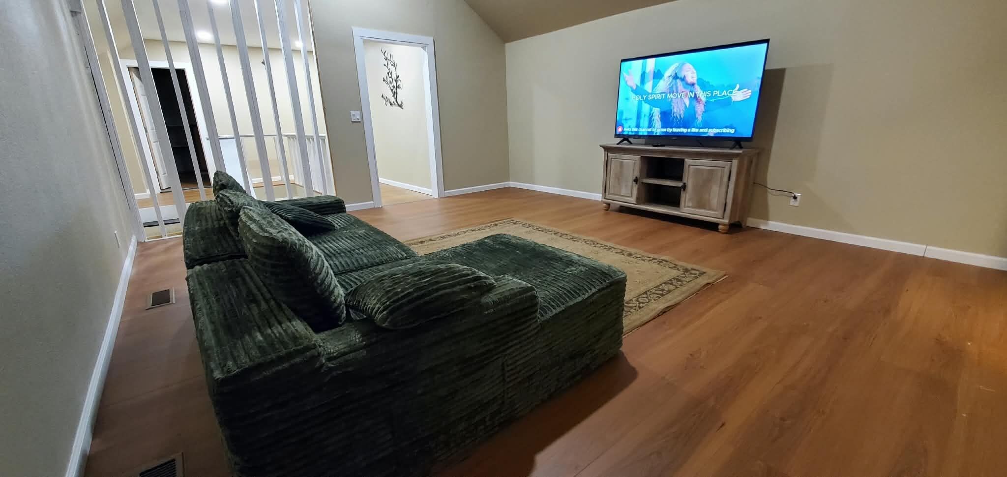 Ein Wohnzimmer mit einem grünen Sofa, einem Fernseher auf einem Holzgestell und einem gemusterten Teppich.