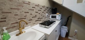 Eine kleine Küchenzeile mit einer weißen Arbeitsplatte, einem Gasherd, einer Mikrowelle und einem Waschbecken mit goldenem Wasserhahn.