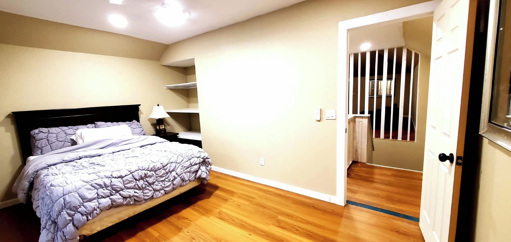 Ein Schlafzimmer mit einem Bett, einem Nachttisch, einer Lampe und einer Tür, die zu einer Treppe führt.