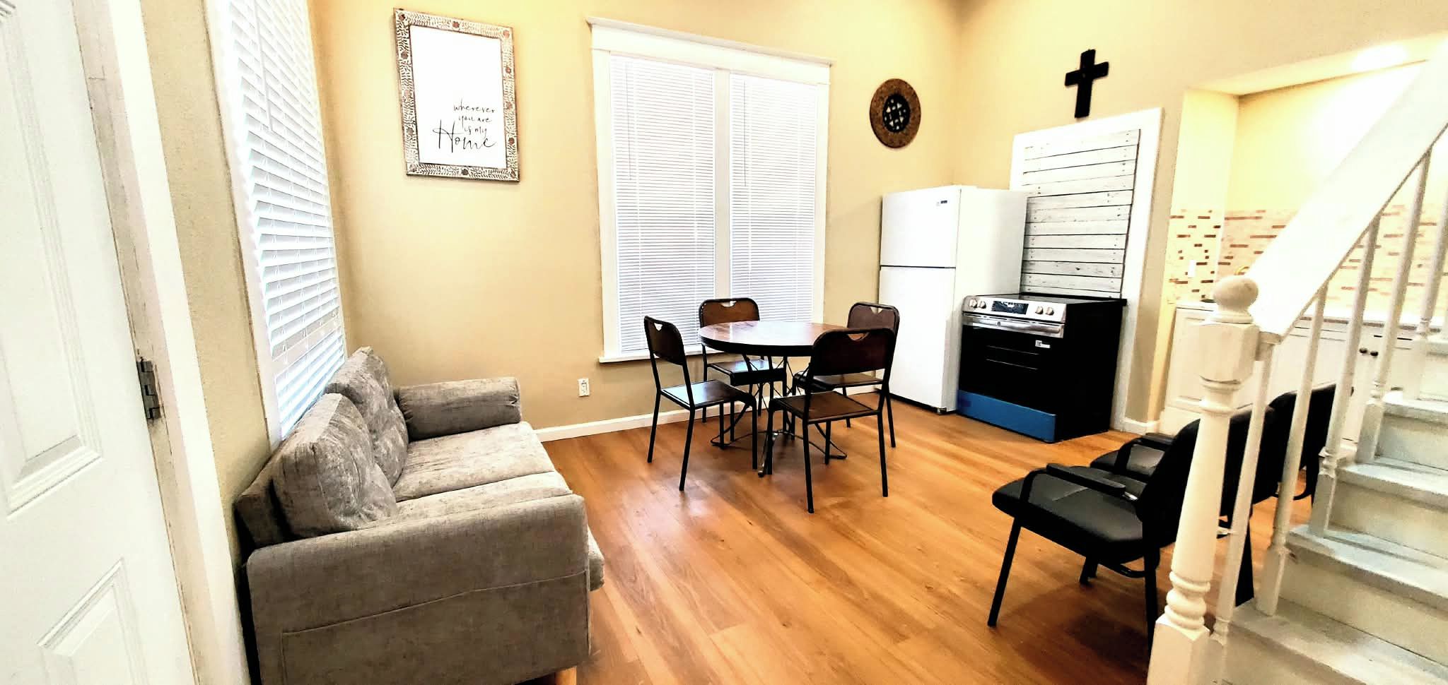 A compact living space with a sofa, dining table, chairs, a kitchen area with a stove, and a staircase.