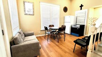 A compact living space with a sofa, dining table, chairs, a kitchen area with a stove, and a staircase.