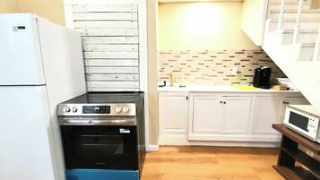 Una cucina compatta con frigorifero, fornello, forno, microonde e mobili bianchi.