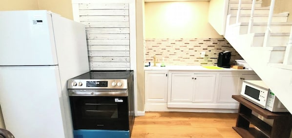 A compact kitchen with a refrigerator, stove, oven, microwave, and white cabinets.