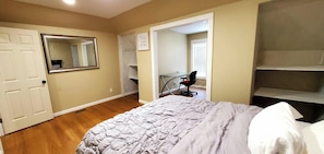 A bedroom with a bed, a door, a mirror, and a desk with a chair.