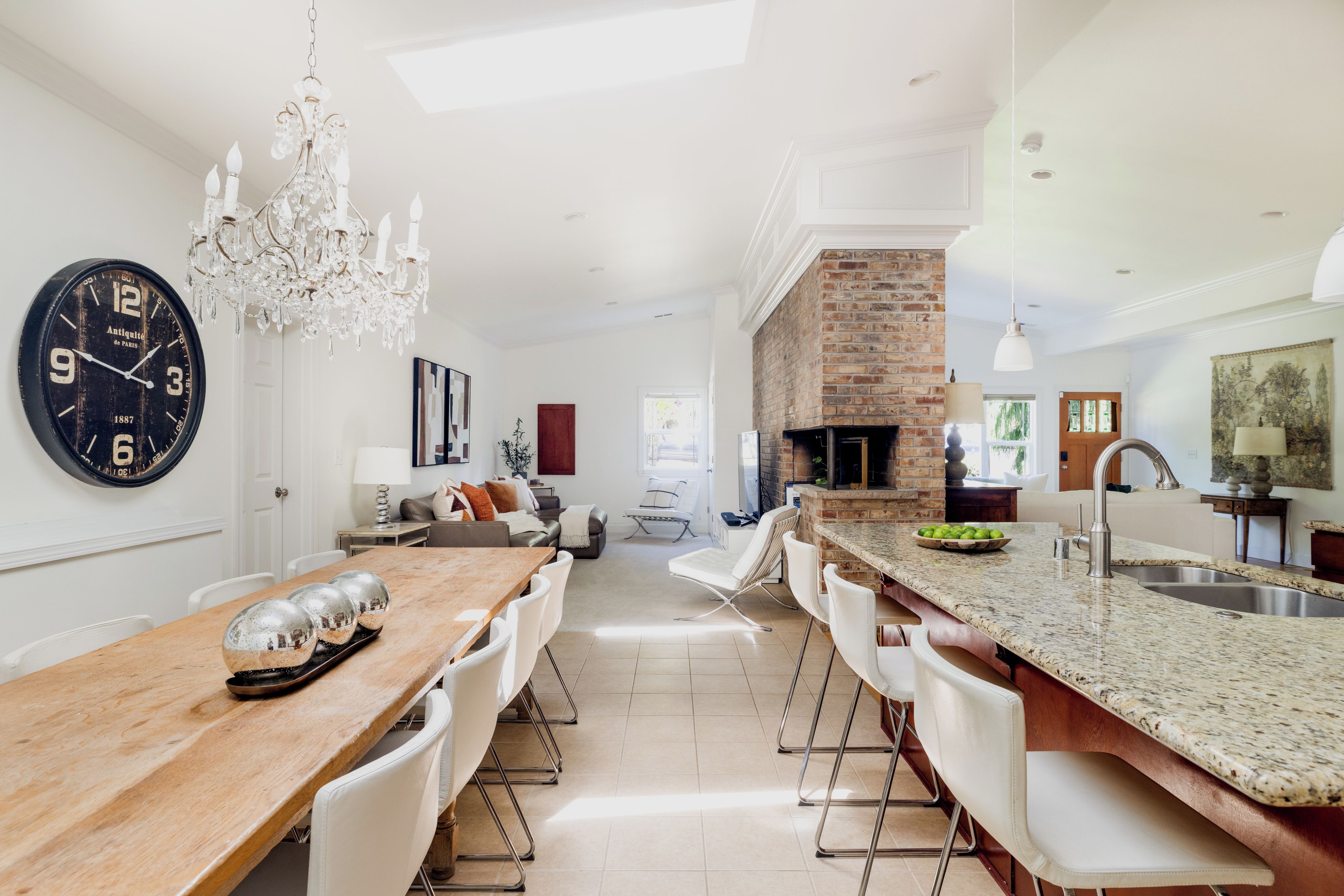 A modern kitchen with a brick fireplace, a chandelier, and a dining area with a wooden table and chairs.