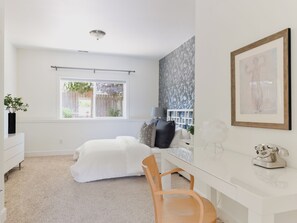 Ein Schlafzimmer mit einem Bett, einem Schreibtisch, einem Stuhl, einem Fenster und einer blumengemusterten Wand.