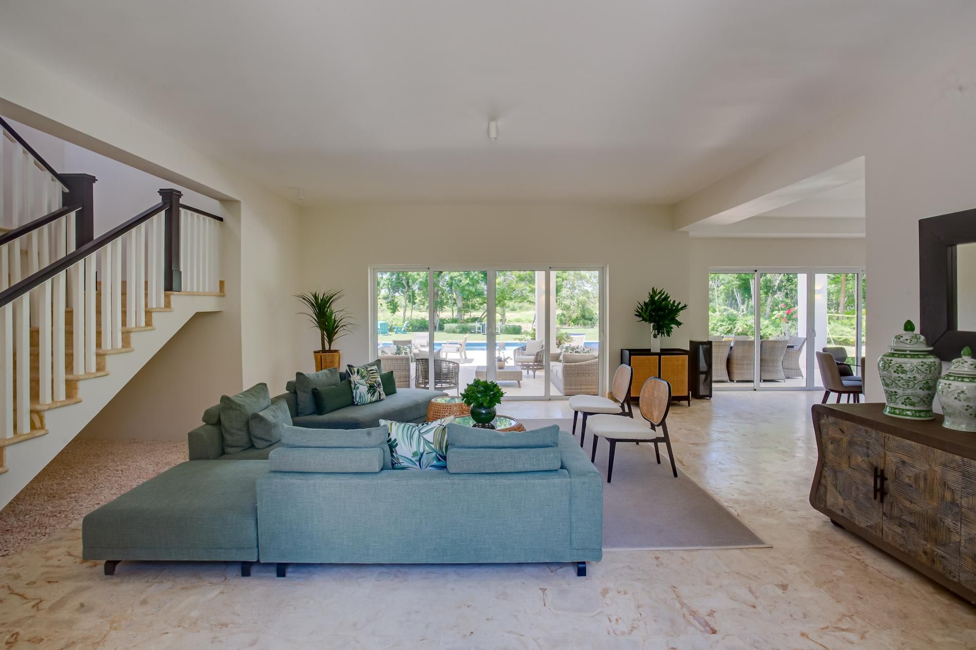 A spacious living area with a large sectional sofa, a staircase, and a view of a pool through large sliding doors.