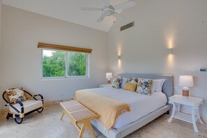 A bedroom with a bed, bedside tables, a chair, a window, and a ceiling fan. - Hacienda A57 - 4BR golf front villa close to beach club (Punta Cana)