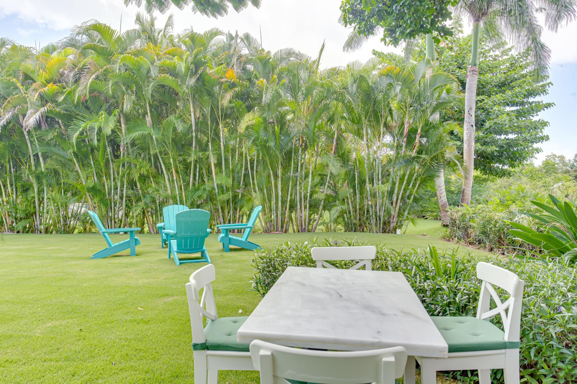 A patio with a white table and chairs, surrounded by lush greenery and tall palm trees.