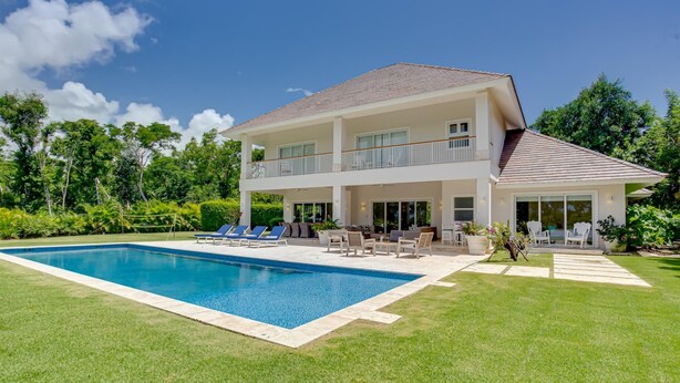 Una casa de dos pisos con piscina, mobiliario exterior y jardín.