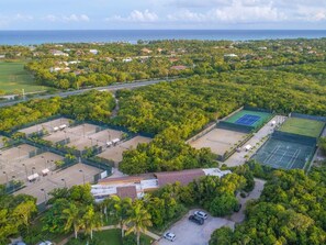 An aerial view of a residential area with multiple tennis courts, a parking lot, and surrounding greenery. - Hacienda A57 - 4BR golf front villa close to beach club (Punta Cana)