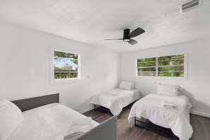 Habitación con dos camas, ventilador de techo y ventanas con vistas a la vegetación.