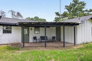 A covered patio area with a table and chairs, a white building with a door, and a grassy yard. - Lakebound House: Ping Pong & Starlink WiFi Near (Somerville)