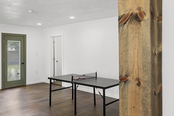 Una habitación con una mesa de ping pong, una puerta con marco verde y una pared blanca.