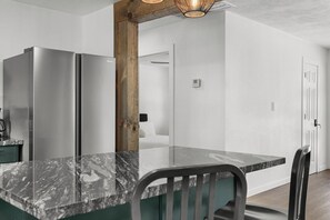 A modern kitchen with two stainless steel refrigerators, a marble countertop, and a dining area with a chair. - Lakebound House: Ping Pong & Starlink WiFi Near (Somerville)