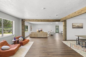Amplia sala de estar con piso de madera, un conjunto de sofás, una mesa de comedor y una cocina al fondo.