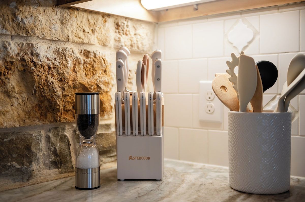 Un plan de travail de cuisine avec un mur en pierre, un récipient en acier inoxydable, un bloc à couteaux et un porte-ustensiles.