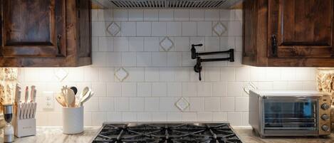 Una cocina con estufa a gas, campana extractora de acero inoxidable y horno tostador.