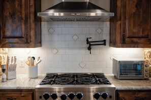 A kitchen with a gas stove, a stainless steel range hood, and a toaster oven. - Hill Country Reunion & Event Estate | Sleeps 28 (Fredericksburg)