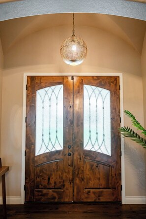 A wooden double door with frosted glass panels and a hanging light fixture above. - Hill Country Reunion & Event Estate | Sleeps 28 (Fredericksburg)