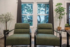 A room with two green upholstered chairs, a potted plant, and a view through a window. - Hill Country Reunion & Event Estate | Sleeps 28 (Fredericksburg)