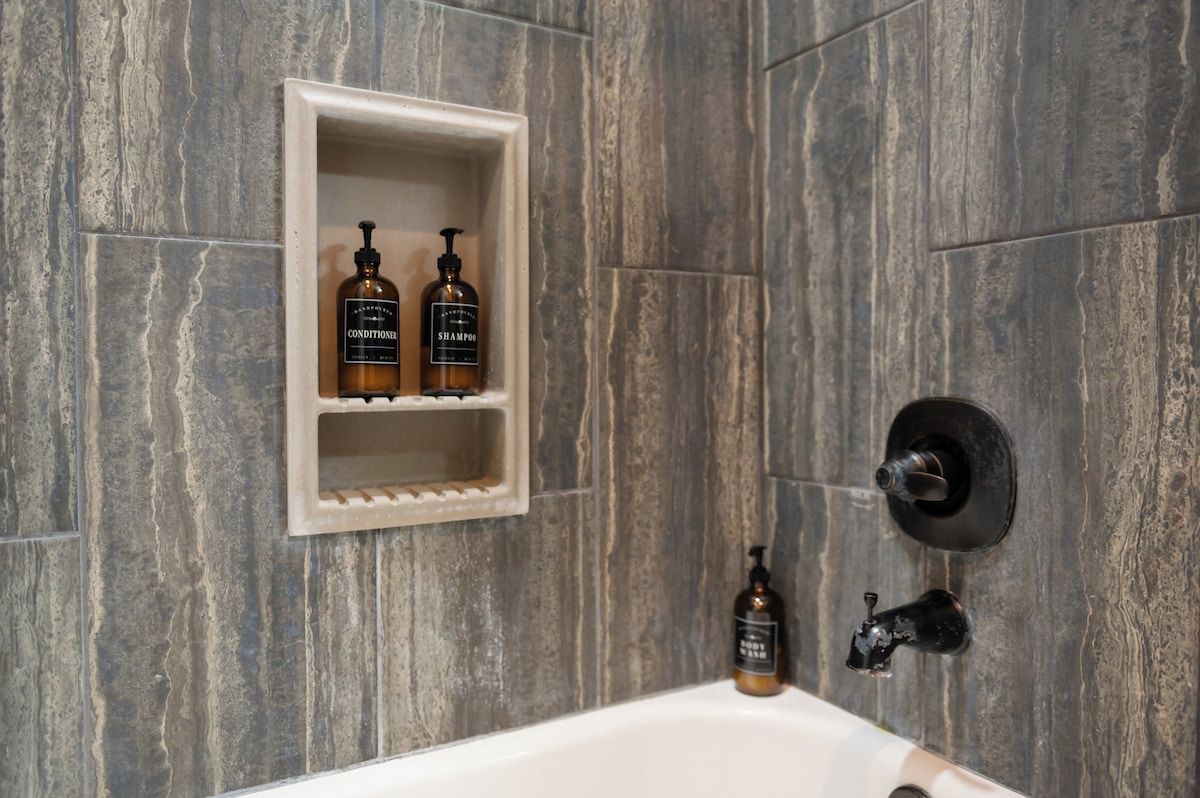 Un baño con estante empotrado que contiene dos botellas de champú y acondicionador.
