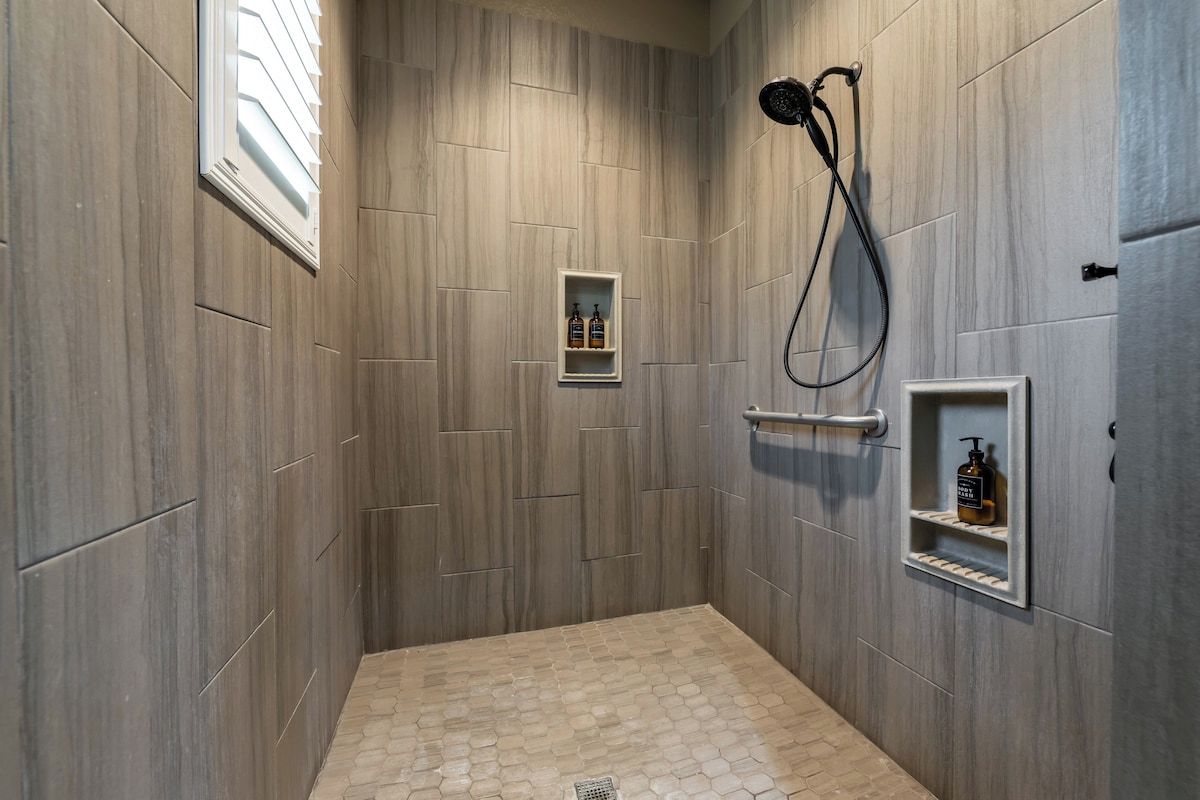 A shower area with a rain showerhead, a towel rack, and two shelves with bottles.