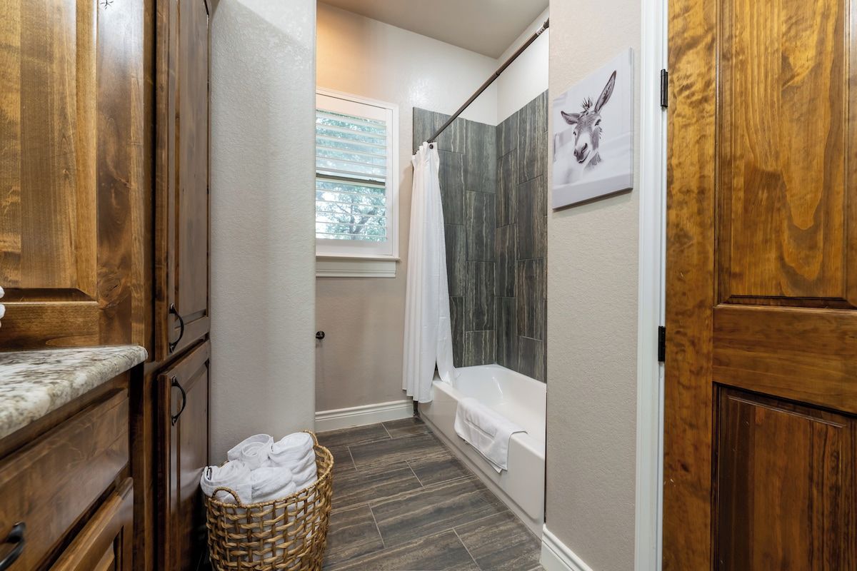 A bathroom with a shower, a bathtub, wooden cabinetry, and a wicker basket with towels.
