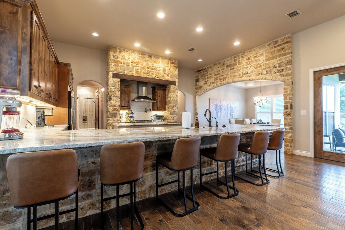 A kitchen with a stone wall, wooden cabinets, and a bar area with stools.